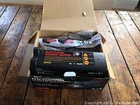 Open cardboard box showing electronic rodent zapper device with labels and attached power cord inside.