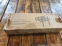 Box of full motion TV wall mount ARL506D-ES REV02 placed on wooden surface, showing brand and model printed on box.
