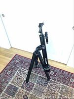 Three angled views of a black Polaris refractor telescope mounted on a black adjustable tripod placed on a patterned rug near a white wall and door.