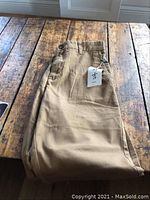 Folded khaki men's pants with tag, laying on a rustic wooden table, showing full length and fabric texture.