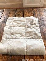 Folded beige Pet Fusion branded cooling blanket on wooden floor.