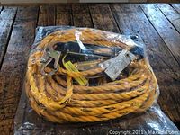 Top-down photo of yellow and black twisted safety rope coiled and packaged in plastic, showing metal shock absorber and large metal hook attachment.