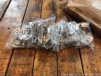 Seven pairs of metal cabinet hinges packaged in clear plastic on wooden surface.