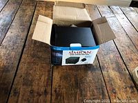 Opened box showing new Simran transformer inside on wooden surface.