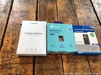 Three boxed network adapters on a wooden table, showing front packaging of each item.