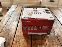 Boxed VTech cordless phone system with four handsets shown from the front on wooden table