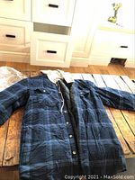 Front view of Wrangler medium plaid work jacket with light-colored hoodie laid flat on a wooden table.
