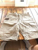 Front view of Wrangler work shorts laid flat on wooden floor, showing full length and pocket details.