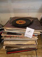 Stack of various vinyl records and albums with one vinyl record on top.