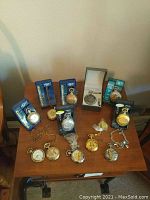 Overview of 12 assorted pocket watches on a wooden table, showcasing various styles and packaging including boxed and plastic-wrapped watches.