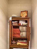 Full view of wooden bathroom cabinet with towels, rugs and decor inside and on top.