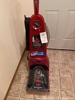 Front view of the Bissell ProHeat carpet cleaner showing controls, hose, and upright design on tiled floor.