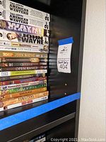 Photo showing close-up of one shelf with old movies and DVDs stacked but contents not included in sale.