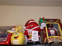 Yellow bunny ears M&M plush, red Santa M&M plush, and Nutcracker Sweet M&M candy dispenser in box on shelf.