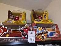 Overview of M&M's Candy Dish Remote Control Holders stacked above limited edition collectible toy vehicles including fire truck and loading zone truck with Red M&M figures