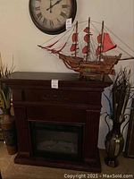 Full view of electric heater fireplace mantle with wooden model ship on top and tall vases on either side