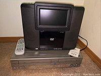 Front view of black portable DVD player on top, silver Emerson VHS DVD combo recorder below, remote control visible on top of recorder