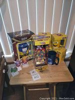 Photo showing all M&M collectibles arranged on a wooden stool in front of window blinds. The photo includes boxed nutcracker, boxed coffee mugs, candy dispensers, and loose character figurines.