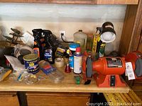 Photo of a table with assorted items including spray cans, a small bottle, wire coil, a can of Planters Cocktail Peanuts, and the Black & Decker bench grinder on the right.