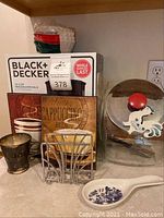 Photo of the boxed Black & Decker coffee maker, decorative coffee sign, metal napkin holder, silver-plated cup, porcelain spoon rest, and metal cookie jar with rooster decoration.