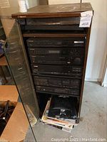 Full view of the wooden cabinet with glass door open showing stacked Pioneer stereo components and storage area with printed materials at the bottom.