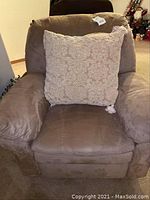 Front view of the brown recliner chair with beige decorative pillow showing padded arms and cushioned seat.