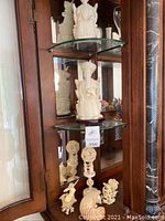 Front and angled view showing the seated Asian woman resin statue and smaller sea life figurines below on glass shelf inside wooden cabinet.