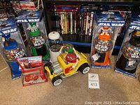 Four Star Wars themed M&M bubblegum machines and a yellow grill toy car with black wheels on carpeted floor with DVDs in background.