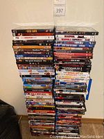 Two tall stacks of assorted DVDs against a beige wall, showing many movie titles.