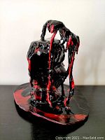 Front view of the black and red glazed sculpture showing the dripping paint effect and the base with artist signature.