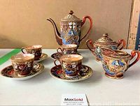 Full set of eleven hand-painted Japanese porcelain tea set pieces including tea pot, four cups, four saucers, creamer, and sugar dish, all decorated with traditional Japanese imagery in browns, blues, and golds.