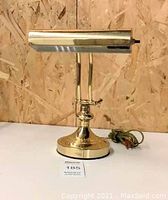 Front view of brass bankers style table lamp showing cylindrical shade, decorative base, and power cord.
