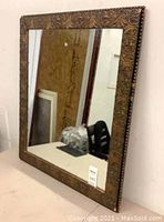 Front angled view of the rectangular antique mirror showing ornate wooden frame with floral and scroll designs and mirror surface.