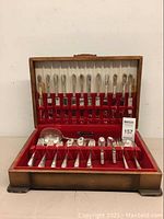 Front view of the open wooden flatware box showing upper and lower compartments filled with silverplated forks, knives, spoons, ladle, and other pieces.