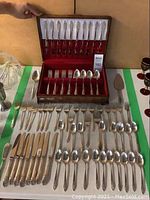 Full 76-piece flatware set arranged showing knives, forks, spoons, and serving utensils along with wooden case.