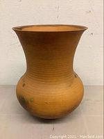 Front view of an orange pottery vase with flared rim and bulbous base, showing fine horizontal ridges and natural variations in color and glaze.