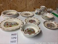 Overview of entire 10-piece Bunnykins dish set showing plates, bowls, and mugs with colorful Bunnykins illustrations and decorative bunny borders.