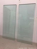 Two clear tempered glass panels standing upright against a wall, showing full front view.