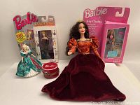 Five Barbie collectibles displayed: porcelain hatbox with porcelain hat (chipped), two Barbie 1996 keychains in original packaging, a 1996 holiday Barbie ornament, and Portuguese princess Barbie doll in red velvet dress.
