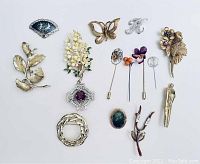 Collection of various vintage brooches and stick pins including silver and gold tones, featuring floral and initial letter designs.