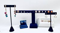 View of various costume earrings displayed on blue and white earring holders showing a variety of dangle hook and post styles and colors.