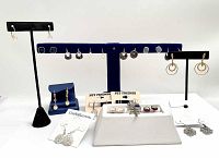 Multiple pairs of earrings displayed on stands and card holders. Variety of designs and styles including drop earrings, hoop earrings, and stud earrings.