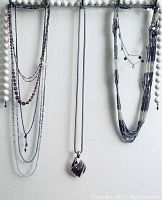 View of all necklaces hanging on a white wooden stand with beads in the background, showing variety of styles and pendant details