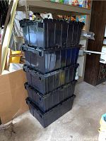 Stack of five black Farmplastic storage totes with interlocking lids showing front and sides of totes.