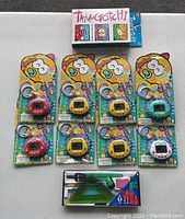Overhead view showing one Tamagotchi box at top, eight DinkiDino packaged devices below, Alvin school set at bottom.