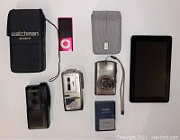 Full lot showing Sony Watchman, Olympus Pearlcorders, Canon Powershot camera and battery pack, Amazon Kindle, and pink iPod Nano
