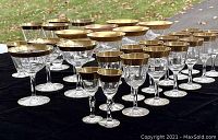 Full view of various stemware pieces arranged on a black surface outdoors showing multiple types and sizes with gold leaf trim.