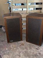 Pair of vintage KLH speakers standing on floor, wooden finish with fabric covered front and KLH logo visible.