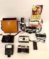 Overview of all vintage cameras and flash units including DeJur movie camera in leather case, Kodak Instamatics, Rollei 35 TE, Nikon and Canon flashes, flash cubes, Lynx trigger.