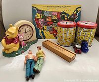Photo showing the vintage collection including Winnie the Pooh battery operated clock with Piglet, US map puzzle, two US states coin banks, Pick-Up Sticks game box, two plastic figures, and two toy cars.